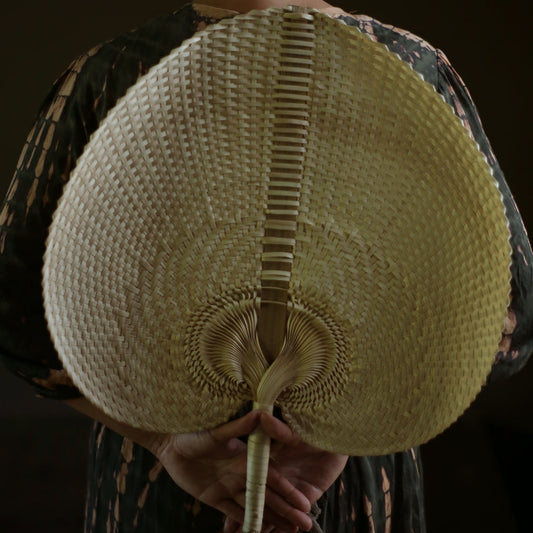 Handwoven lightweight fan for hot flashes made from natural materials held behind a person