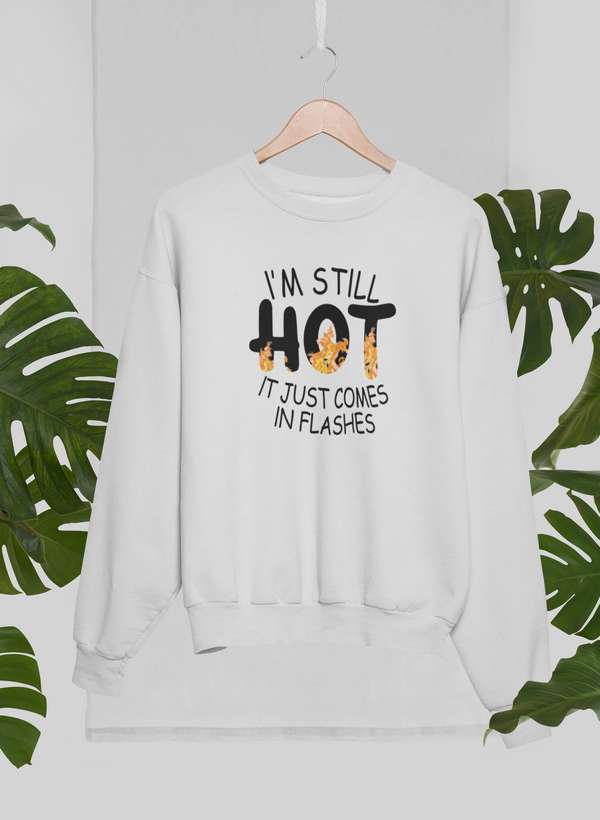 White sweatshirt with menopause sweatshirt humor text on hanger surrounded by green leaves